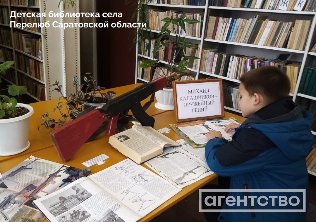 A child reading books on the AK-47 and other weaponry beneath a sign that reads "Mikhail Kalashnikov — Weapons Genius." The image was captured in a children's library in the village of Perelyub in Russia's Saratov Region / Source: Agentstvo