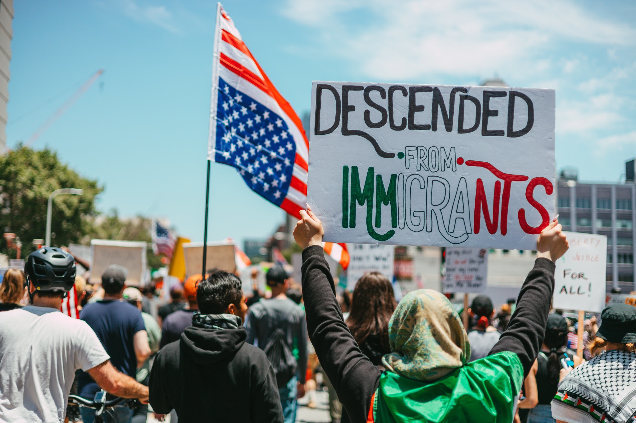 Protesters march in Downtown Los Angeles for the "No Kings" protest on June 14, 2025. A sign reads "Descended from Immigrants."