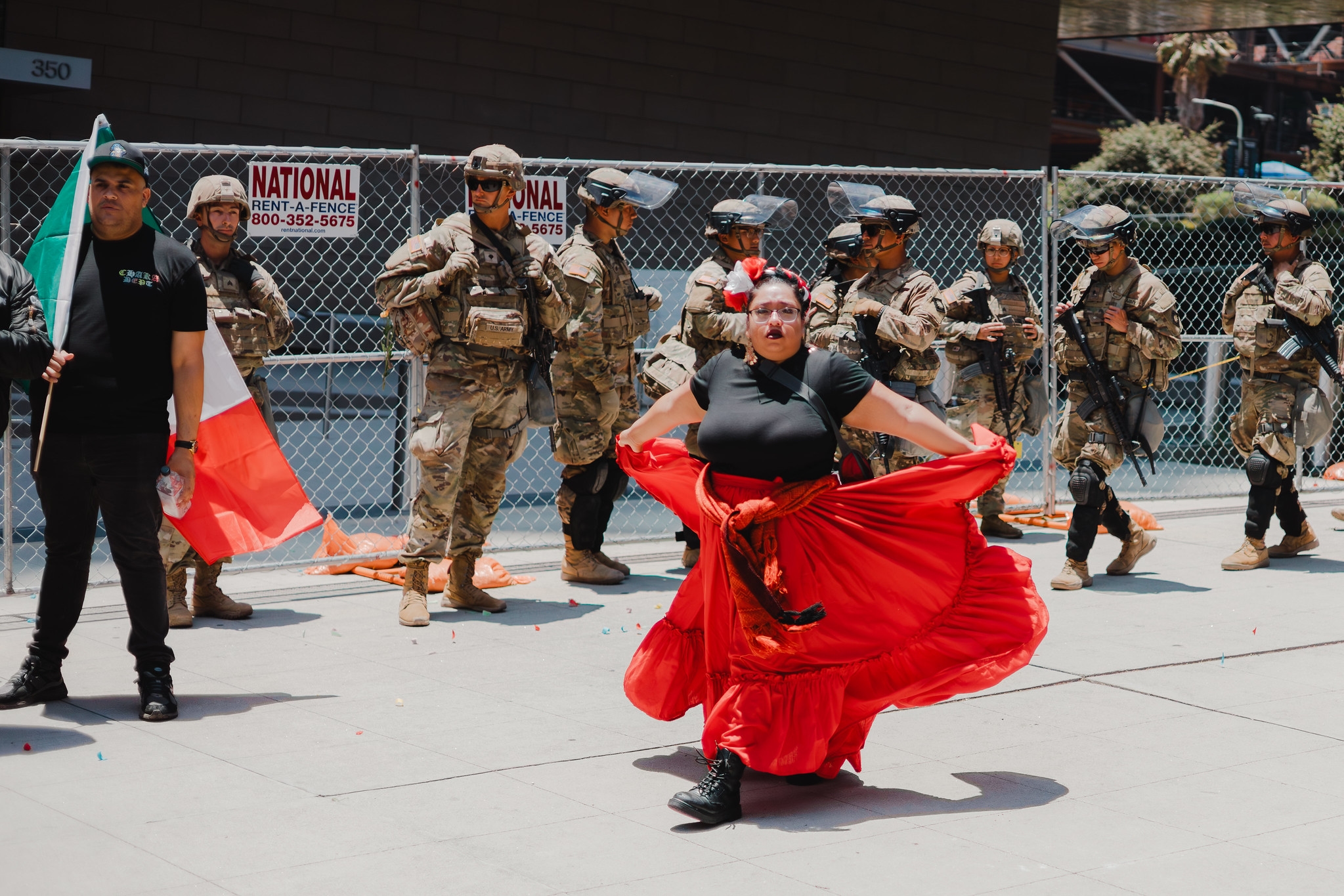 A woman with a red skirt walks in front of a line of armed troops in Downtown Los Angeles for the "No Kings" protest on June 14, 2025.