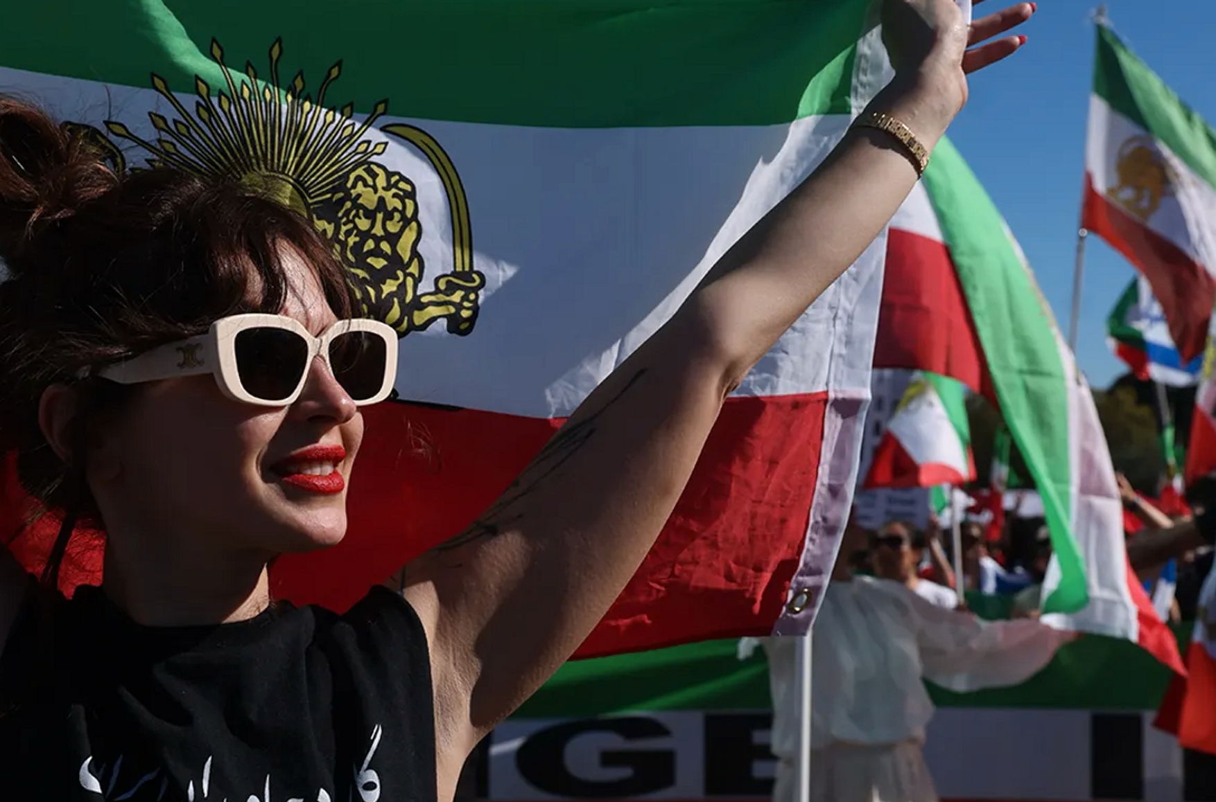 A woman holds up an Iranian Lion and Sun flag as people celebrate the death of Ayatollah Khamenei in Los Angeles. Photo: Genaro Molina / Los Angeles Times