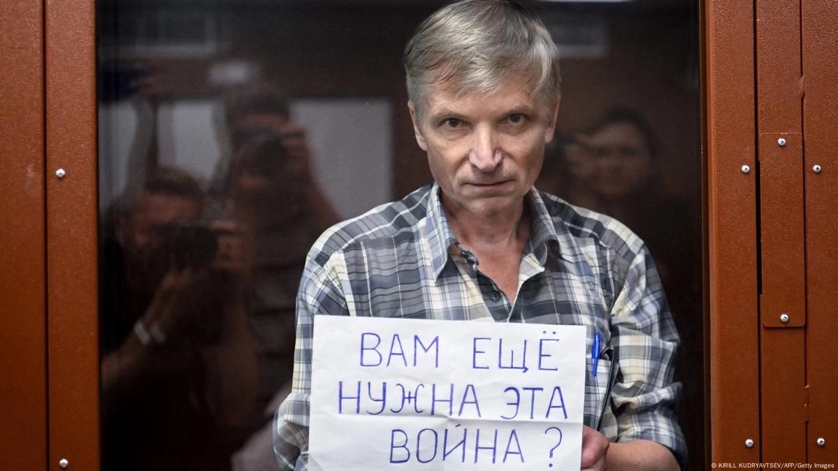 Gorinov, pictured in a courtroom holding cell, holding up a sheet of paper reading “Do you still need this war?”