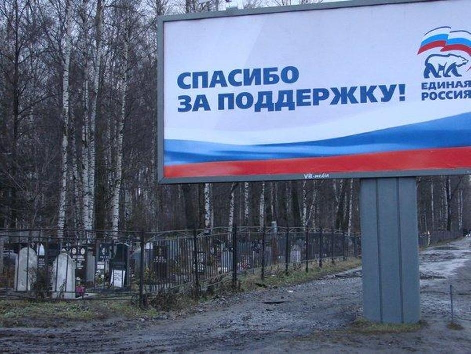 A billboard for Vladimir Putin's United Russia party that reads «Спасибо за поддержку!» (Thank you for your support!) placed directly next to a fenced cemetery