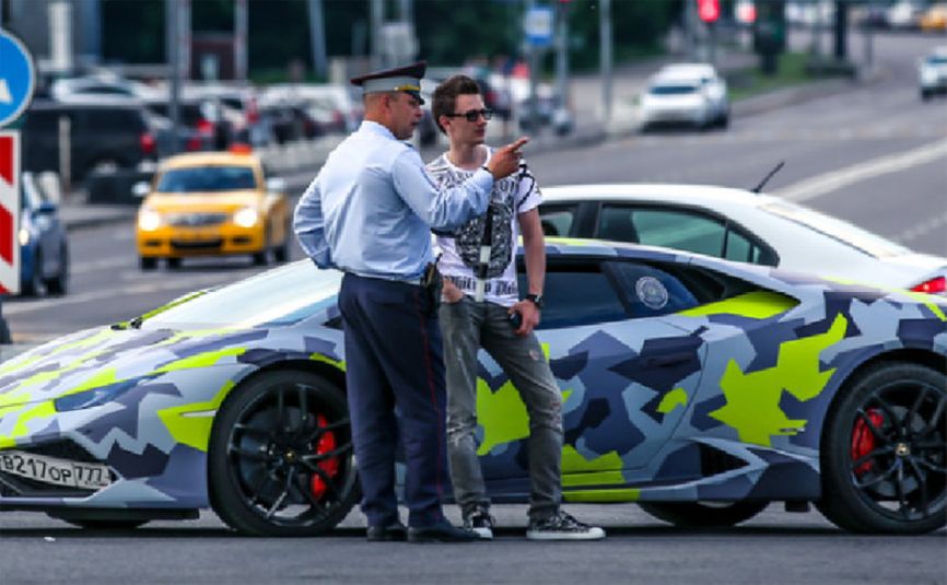 Evil Corp leader Maksim Yakubets talks to a Russian policeman in front of his Lamborghini with the license plate “VOR” (lit. “THIEF”)